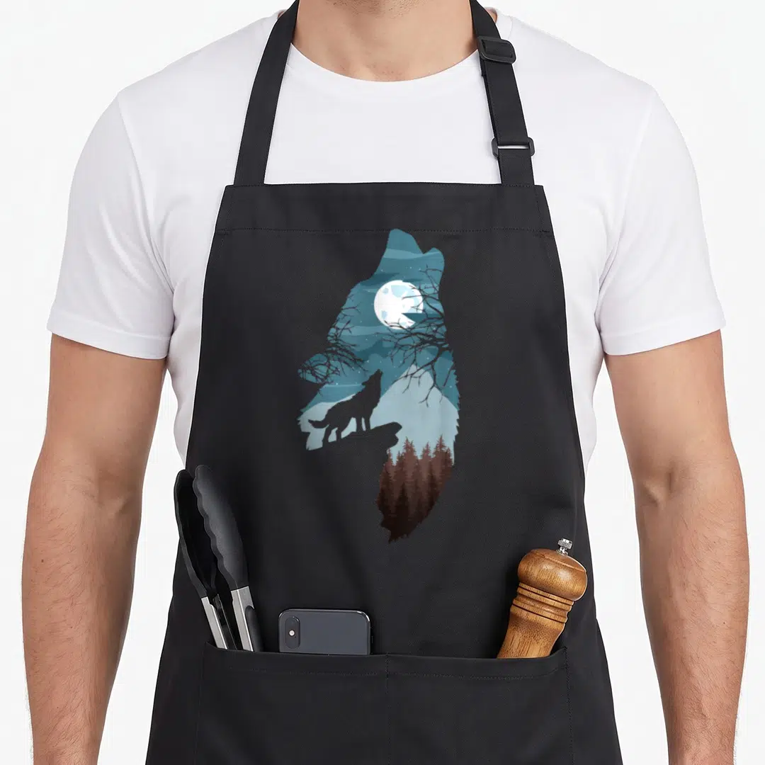 Forest full moon apron - Wolf silhouette containing moon, mountains, and forest scene in blue and brown — shown on a black cotton canvas apron against a white background