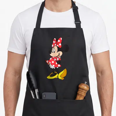 Pose polka dot apron - Minnie Mouse in red polka dot dress and yellow shoes standing sideways — shown on a black cotton canvas apron against a white background