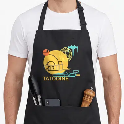 Drawing new hope apron - Yellow circle with building silhouette, blue ship, orange sphere, and TATOOINE text — shown on a black cotton canvas apron against a white background