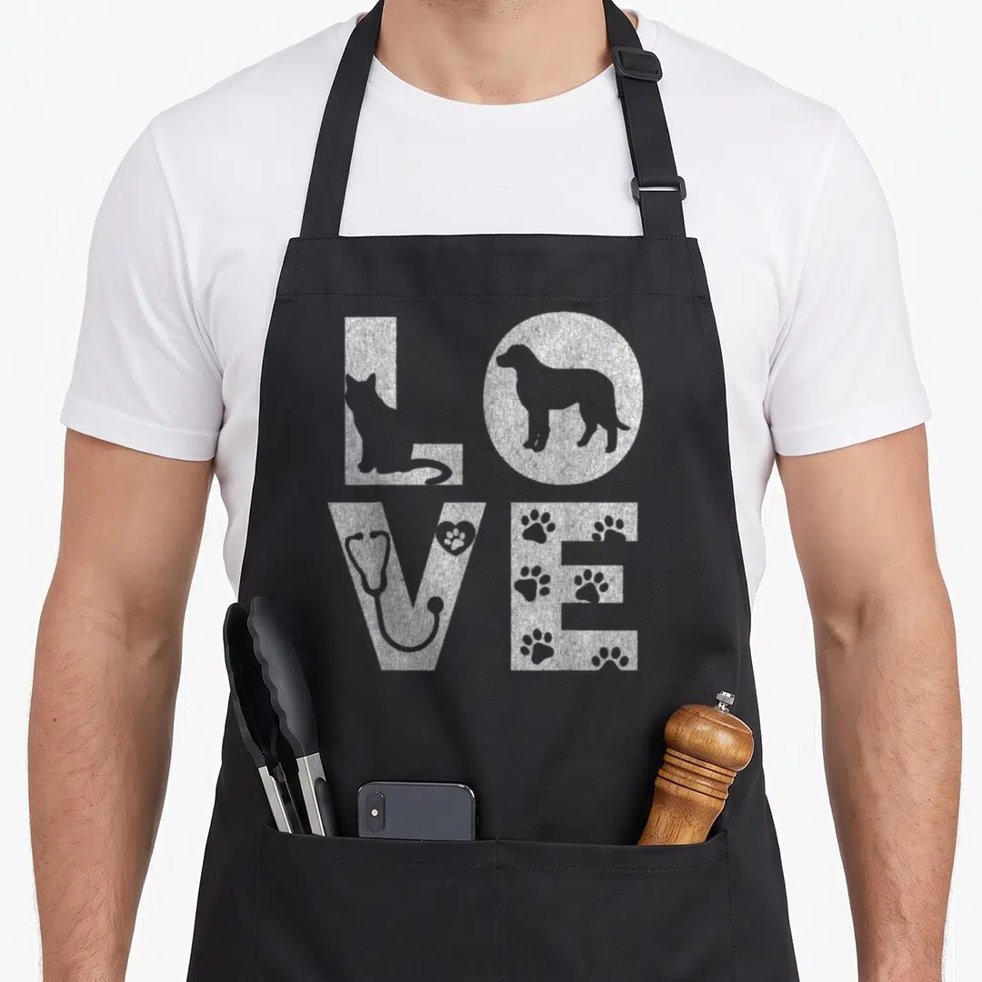 Vet animal apron - White distressed LOVE text with cat, dog, stethoscope, and paw prints inside letters — shown on a black cotton canvas apron against a white background