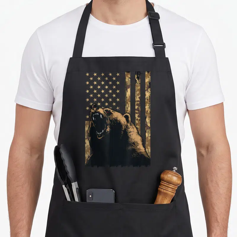 Desert american flag apron - Roaring bear silhouette over distressed stars and vertical desert camo stripes in black — shown on a black cotton canvas apron against a white background