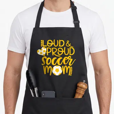 Loud day football apron - Yellow stacked text LOUD PROUD soccer mom with heart and round soccer balls — shown on a black cotton canvas apron against a white background
