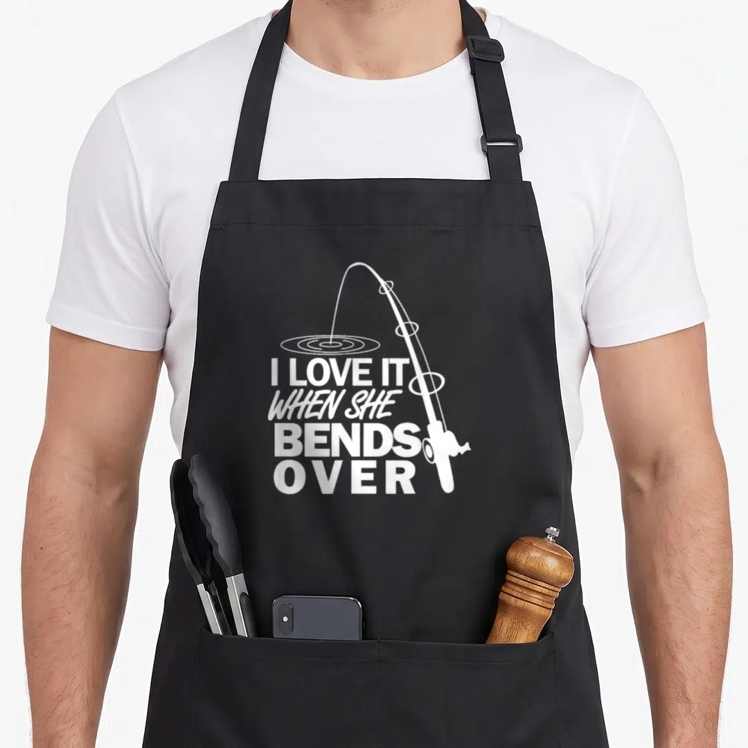 Bend fishing aprons - White bent fishing rod with ripples and stacked text I LOVE IT WHEN SHE BENDS — shown on a black cotton canvas apron against a white background