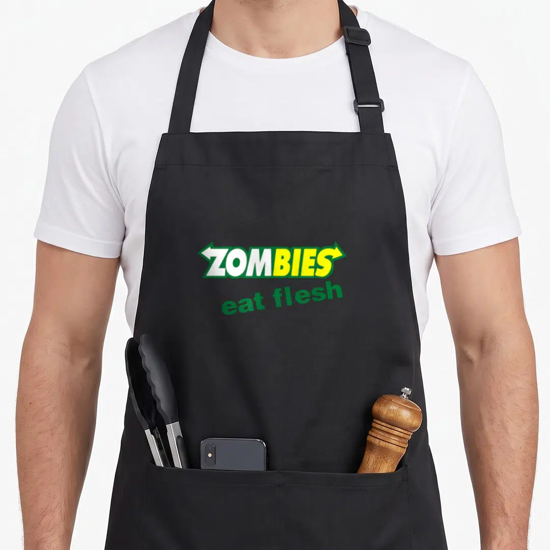 Eat halloween apron - ZOMBIES eat flesh text in green yellow white arrow banner typography — shown on a black cotton canvas apron against a white background