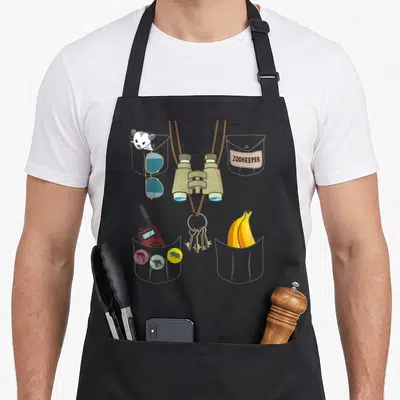 Explorer halloween apron - Cartoon zookeeper vest with binoculars, keys, walkie talkie, sunglasses, banana, and mouse — shown on a black cotton canvas apron against a white background
