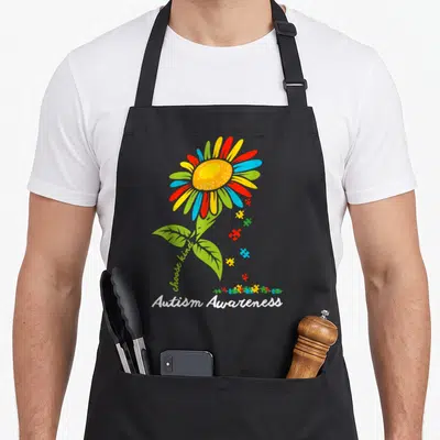 Autism sunflower apron - Multicolored flower with puzzle pieces and choose kind text above Autism Awareness lettering — shown on a black cotton canvas apron against a white background