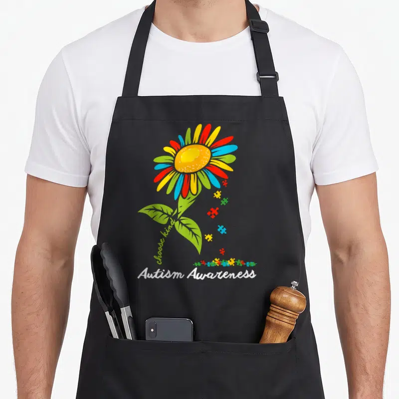 Autism sunflower apron - Multicolored flower with puzzle pieces and choose kind text above Autism Awareness lettering — shown on a black cotton canvas apron against a white background