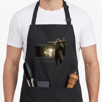 Village video game apron - Karl Heisenberg character holding a hammer in sepia with gold text — shown on a black cotton canvas apron against a white background