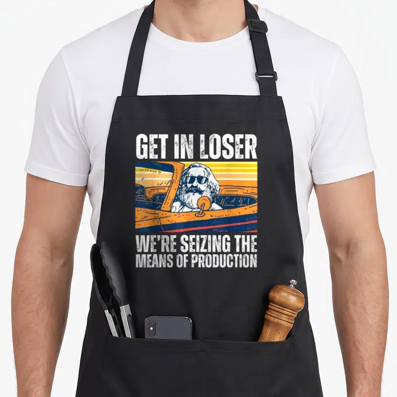 Seizing get loser apron - Karl Marx in retro car with white text GET IN LOSER and orange blue yellow stripes — shown on a black cotton canvas apron against a white background