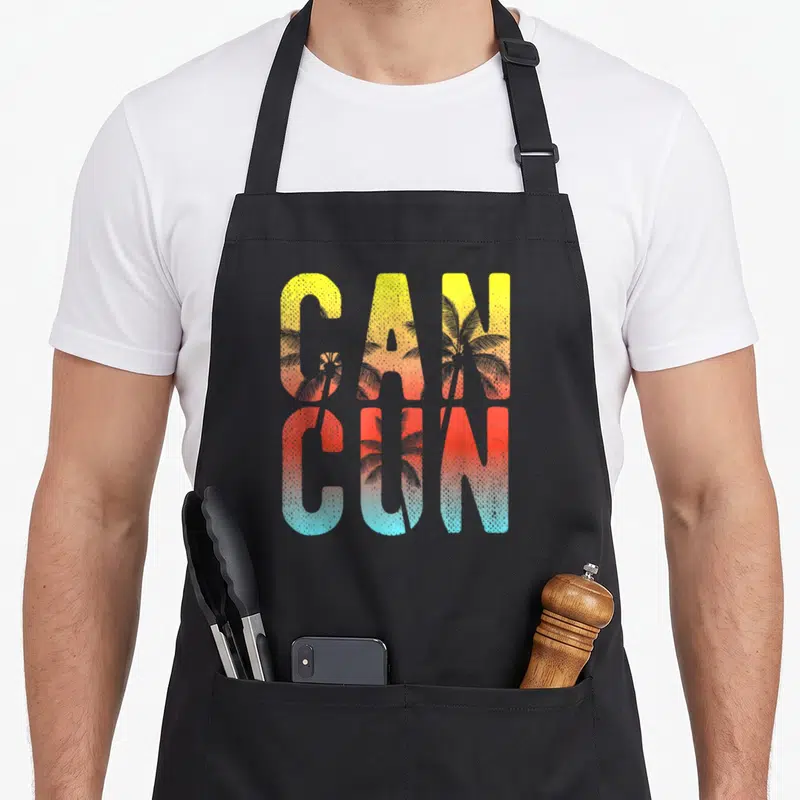 Cancun souvenir mexico apron - Stacked CAN CUN text with palm tree silhouettes in yellow orange red and light blue — shown on a black cotton canvas apron against a white background