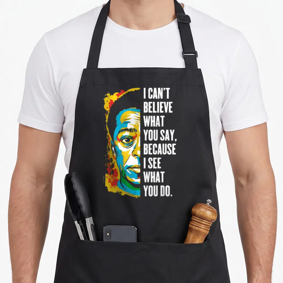 Jame black history apron - Pop art portrait of James Baldwin next to stacked white text I can't believe what you say — shown on a black cotton canvas apron against a white background