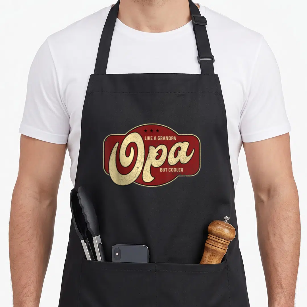 Opa but grandpa apron - Red badge with beige Opa text and three black stars — shown on a black cotton canvas apron against a white background