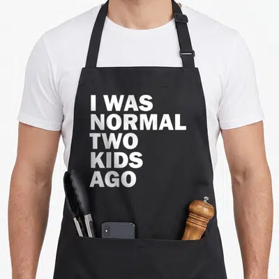 Normal father day apron - White stacked text reading I WAS NORMAL TWO KIDS AGO — shown on a black cotton canvas apron against a white background