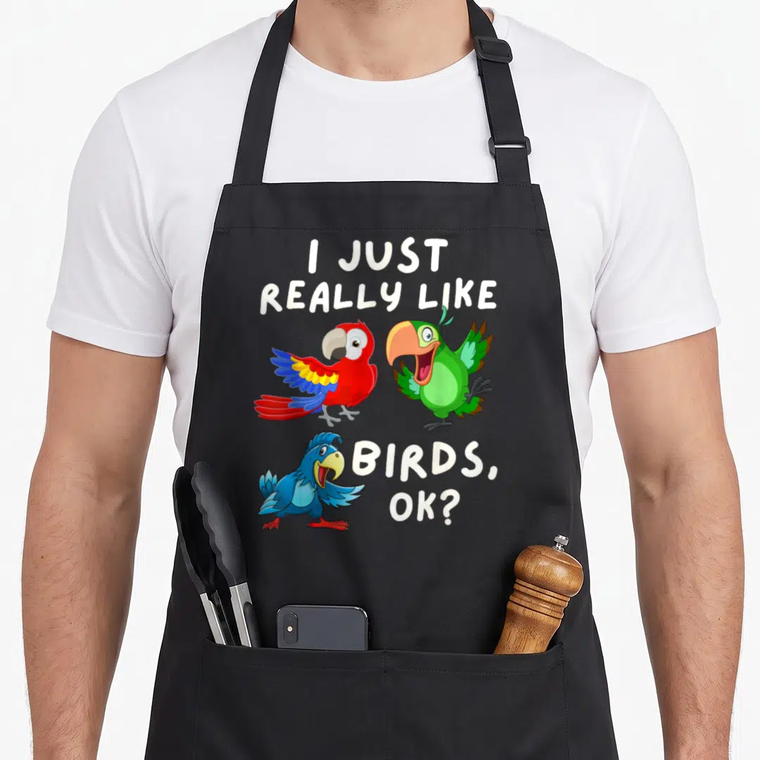 Fan bird apron - Three cartoon parrots in red green and blue with white text reading I just really like birds ok — shown on a black cotton canvas apron against a white background