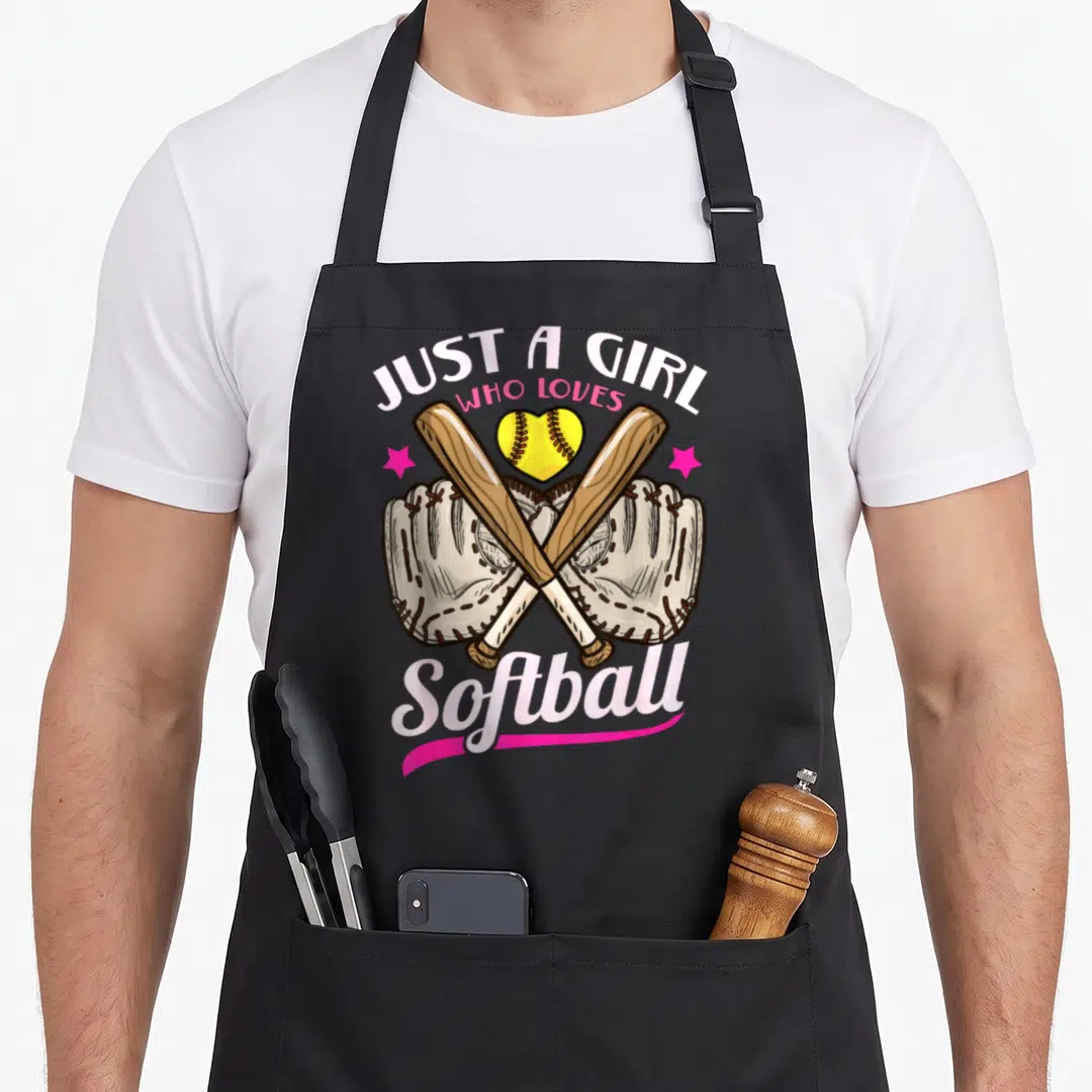 Funny softball player apron - Crossed bats, two mitts, heart softball, pink stars, and text JUST A GIRL WHO LOVES — shown on a black cotton canvas apron against a white background