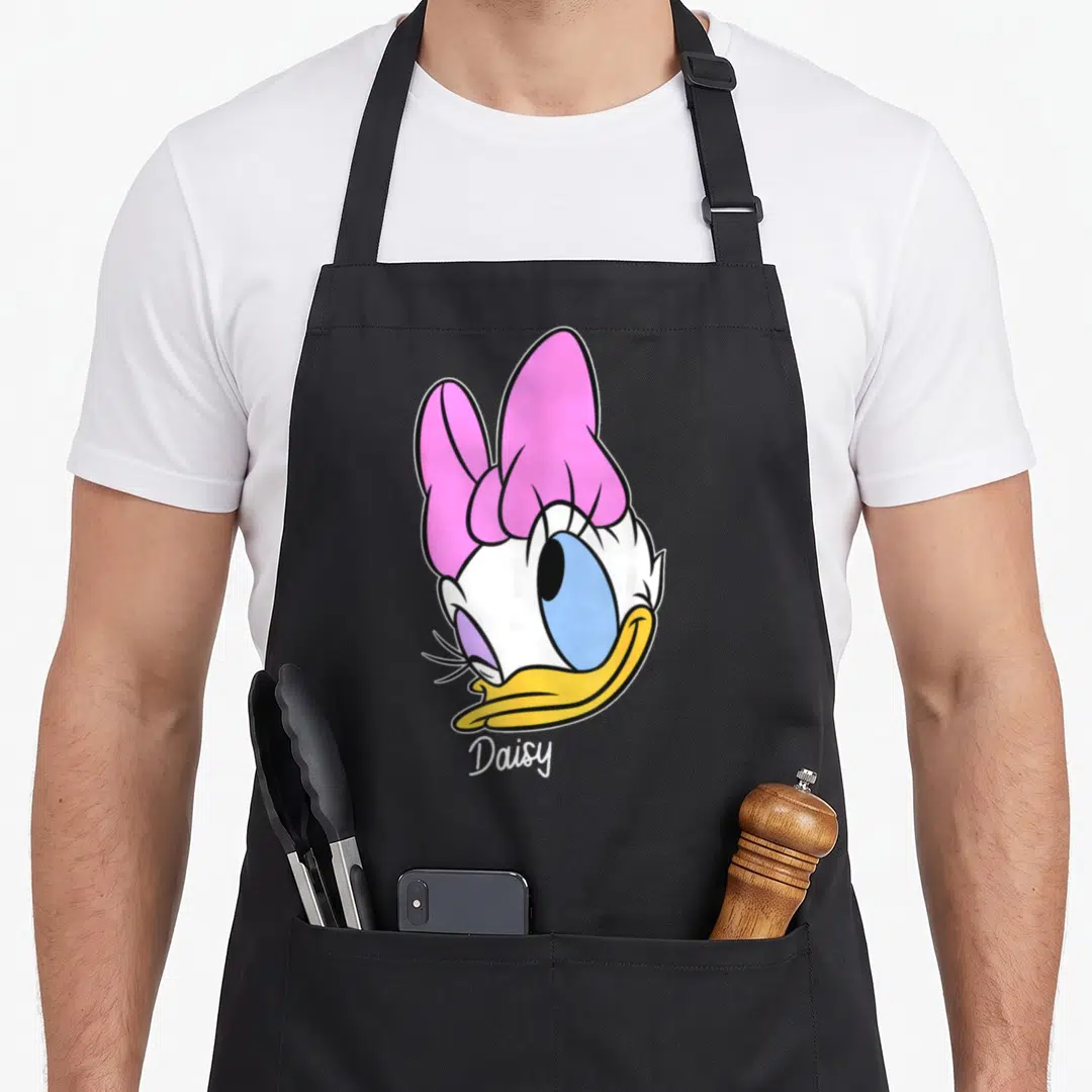 Friend face daisy apron - Cartoon duck head with pink bow and white Daisy text — shown on a black cotton canvas apron against a white background