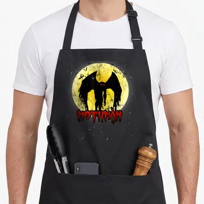 Moon bat apron - Black Mothman silhouette before yellow moon with red MOTHMAN text and small bats — shown on a black cotton canvas apron against a white background