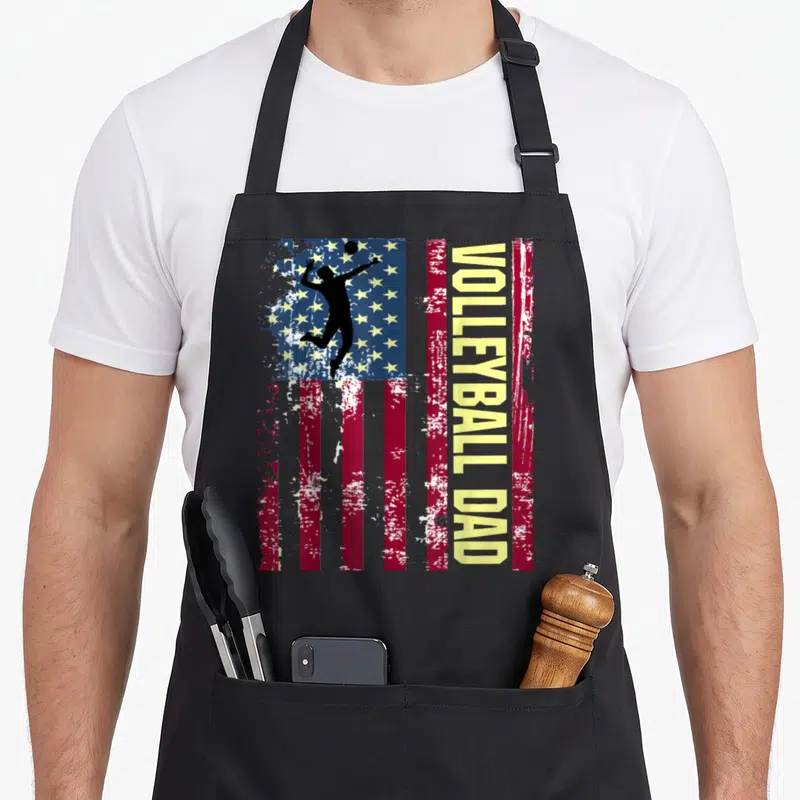 Funny volleyball american flag apron - Vertical distressed US flag with black volleyball player silhouette and yellow — shown on a black cotton canvas apron against a white background