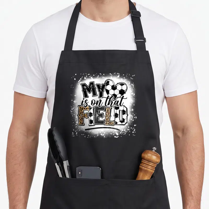 Field leopard apron - MY is on that FIELD text with soccer heart and mixed pattern letters — shown on a black cotton canvas apron against a white background