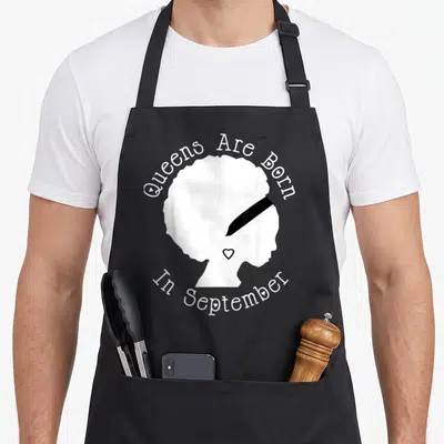 September african american aprons - White afro silhouette with Queens Are Born In September text and heart detail — shown on a black cotton canvas apron against a white background