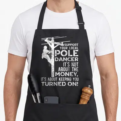 Dancer utility apron - Distressed white lineman climbing utility pole with text about keeping you turned — shown on a black cotton canvas apron against a white background