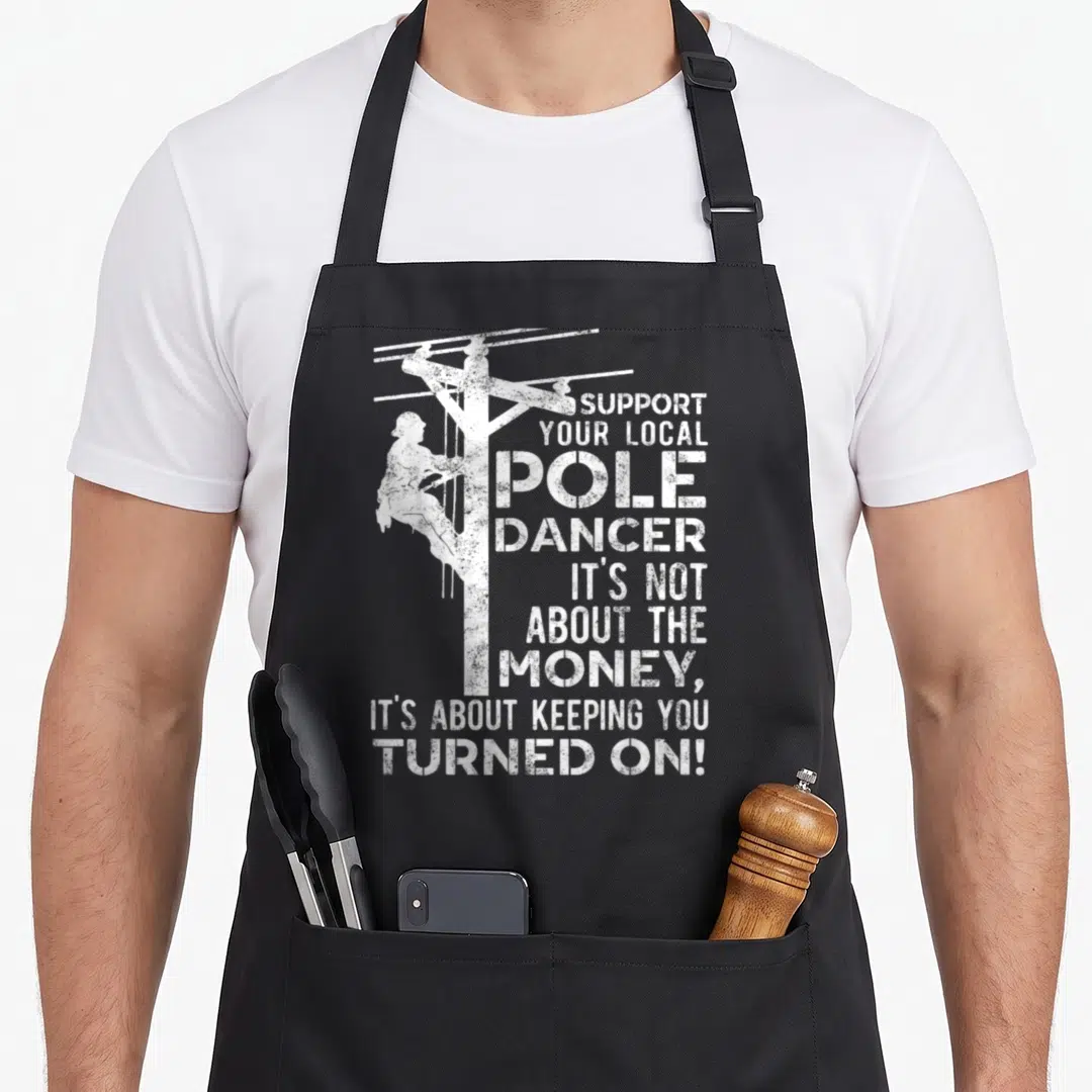 Dancer utility apron - Distressed white lineman climbing utility pole with text about keeping you turned — shown on a black cotton canvas apron against a white background