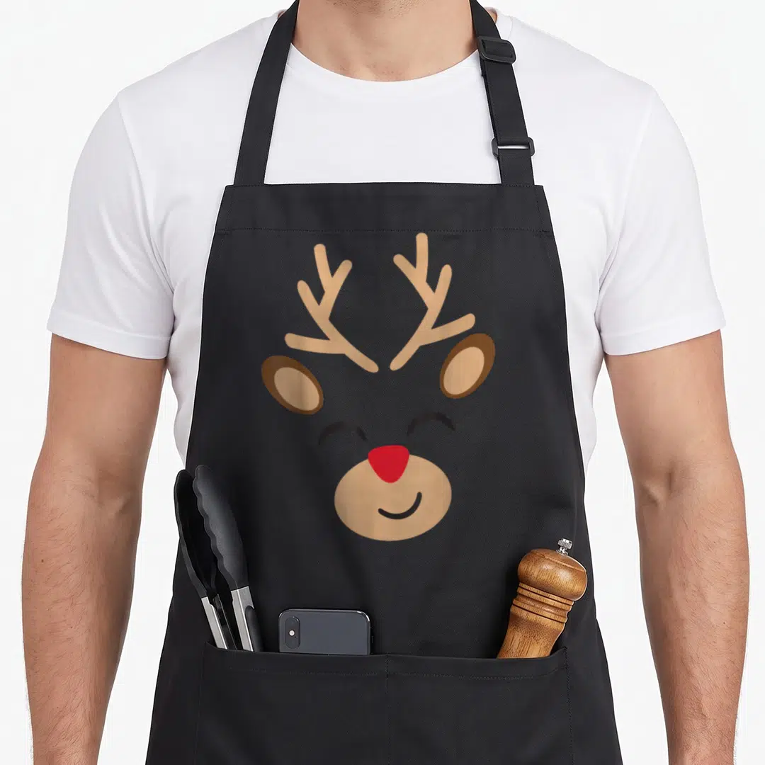 Adorable reindeer apron - Cartoon reindeer face with tan antlers, brown ears, red nose, and black smile — shown on a black cotton canvas apron against a white background