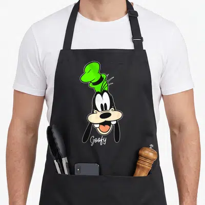 Face friends apron - Cartoon head of Goofy in green hat with script text below chin — shown on a black cotton canvas apron against a white background
