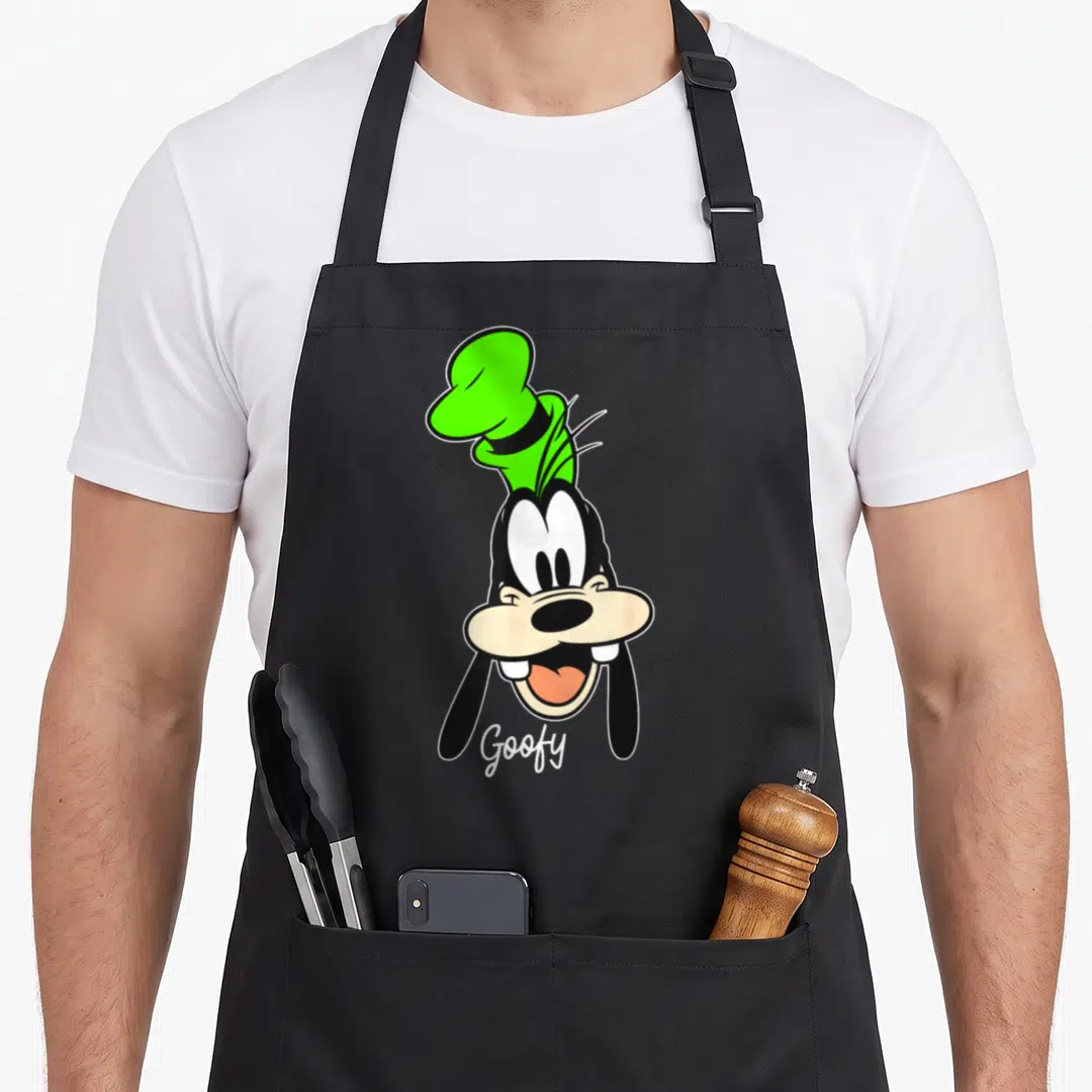 Face friends apron - Cartoon head of Goofy in green hat with script text below chin — shown on a black cotton canvas apron against a white background