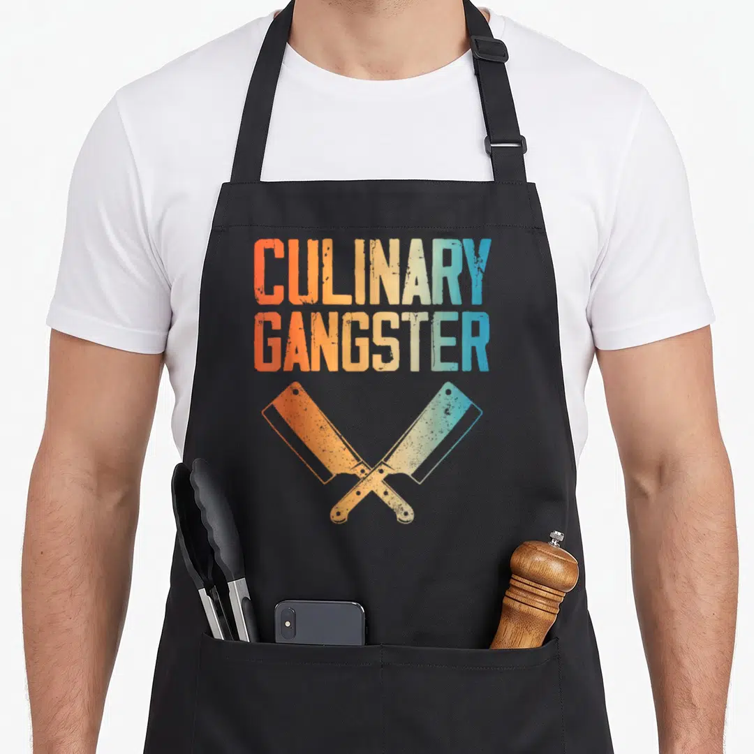 Sous culinary aprons - Crossed cleavers in orange yellow and blue below distressed CULINARY GANGSTER text — shown on a black cotton canvas apron against a white background