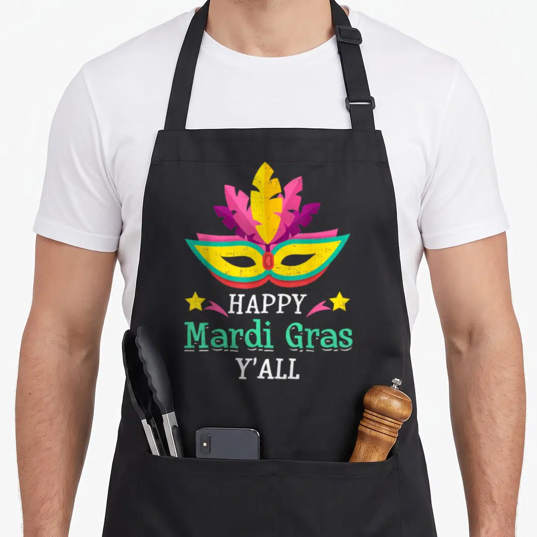 Yall fat chef apron - Retro masquerade mask in yellow pink purple and mint with stars and Happy Mardi Gras Y'all text — shown on a black cotton canvas apron against a white background