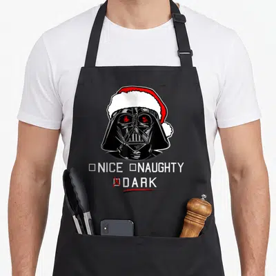 Dark santa apron - Darth Vader in Santa hat with Nice Naughty Dark checklist marked with red X — shown on a black cotton canvas apron against a white background