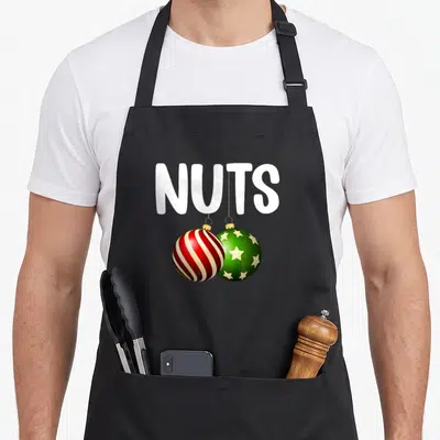 Cute chestnut couples christmas aprons - NUTS text above red striped and green starry Christmas ornaments hanging — shown on a black cotton canvas apron against a white background