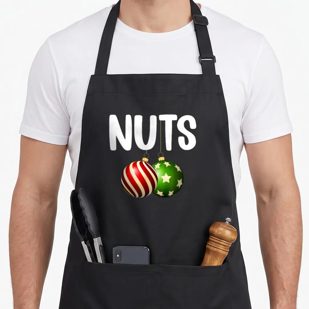 Cute chestnut couples christmas aprons - NUTS text above red striped and green starry Christmas ornaments hanging — shown on a black cotton canvas apron against a white background