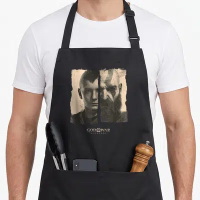 Krato split apron - Two men in cross-hatched line art with centered GOD OF WAR RAGNARÖK text below — shown on a black cotton canvas apron against a white background