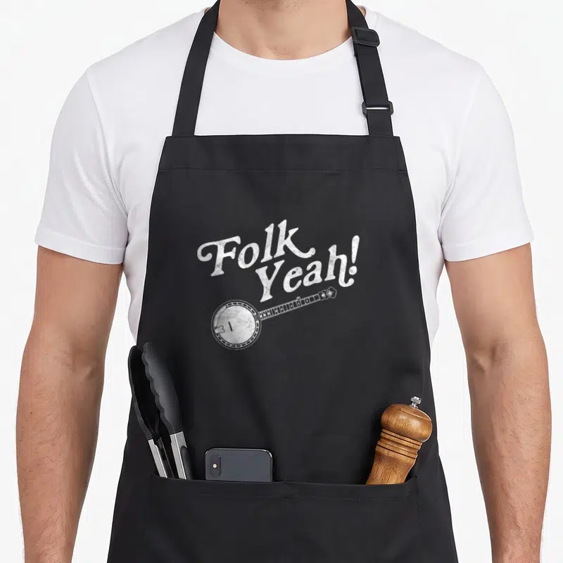 Folk yeah love apron - White distressed Folk Yeah text and banjo graphic on black apron — shown on a black cotton canvas apron against a white background