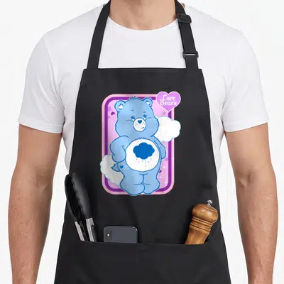 Grumpy care apron - Blue bear with rain cloud belly badge inside pink and purple frame with Care Bears text — shown on a black cotton canvas apron against a white background