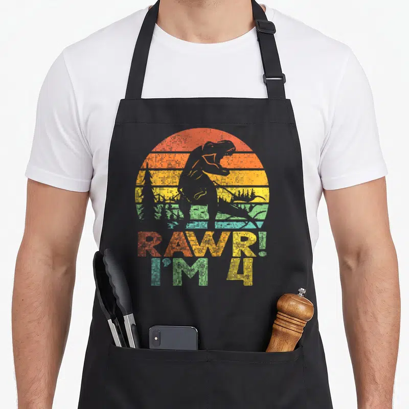 Rawr dinosaur t-rex apron - Grey T-Rex silhouette over orange yellow green blue striped sun with RAWR I M 4 text — shown on a black cotton canvas apron against a white background
