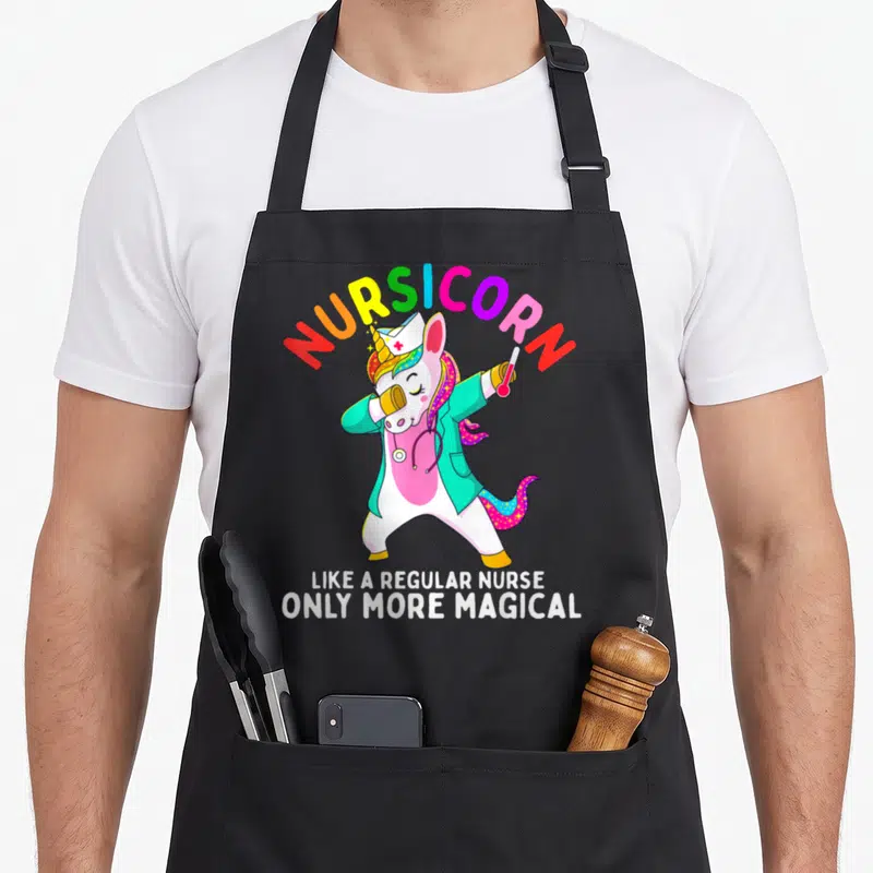 Unicorn nursing apron - Dabbing unicorn nurse in teal coat with Nursicorn rainbow text and white slogan — shown on a black cotton canvas apron against a white background
