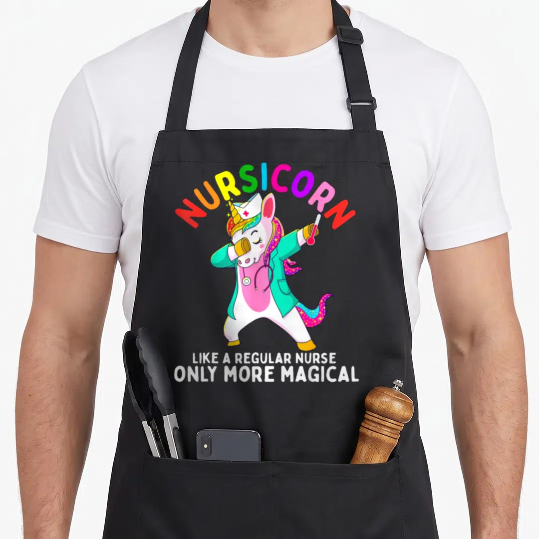 Unicorn nursing apron - Dabbing unicorn nurse in teal coat with Nursicorn rainbow text and white slogan — shown on a black cotton canvas apron against a white background