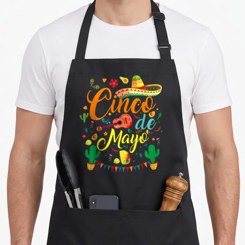 Cinco mayo mexican apron - Cinco de Mayo text with sombrero guitar tacos cacti bunting flags in cartoon style — shown on a black cotton canvas apron against a white background