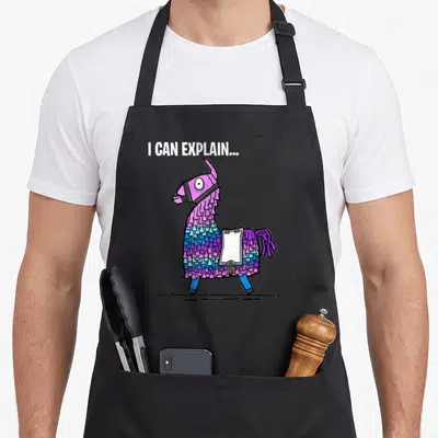 Loot gaming apron - Cartoon llama in purple and blue with muzzle and clipboard under I CAN EXPLAIN text — shown on a black cotton canvas apron against a white background