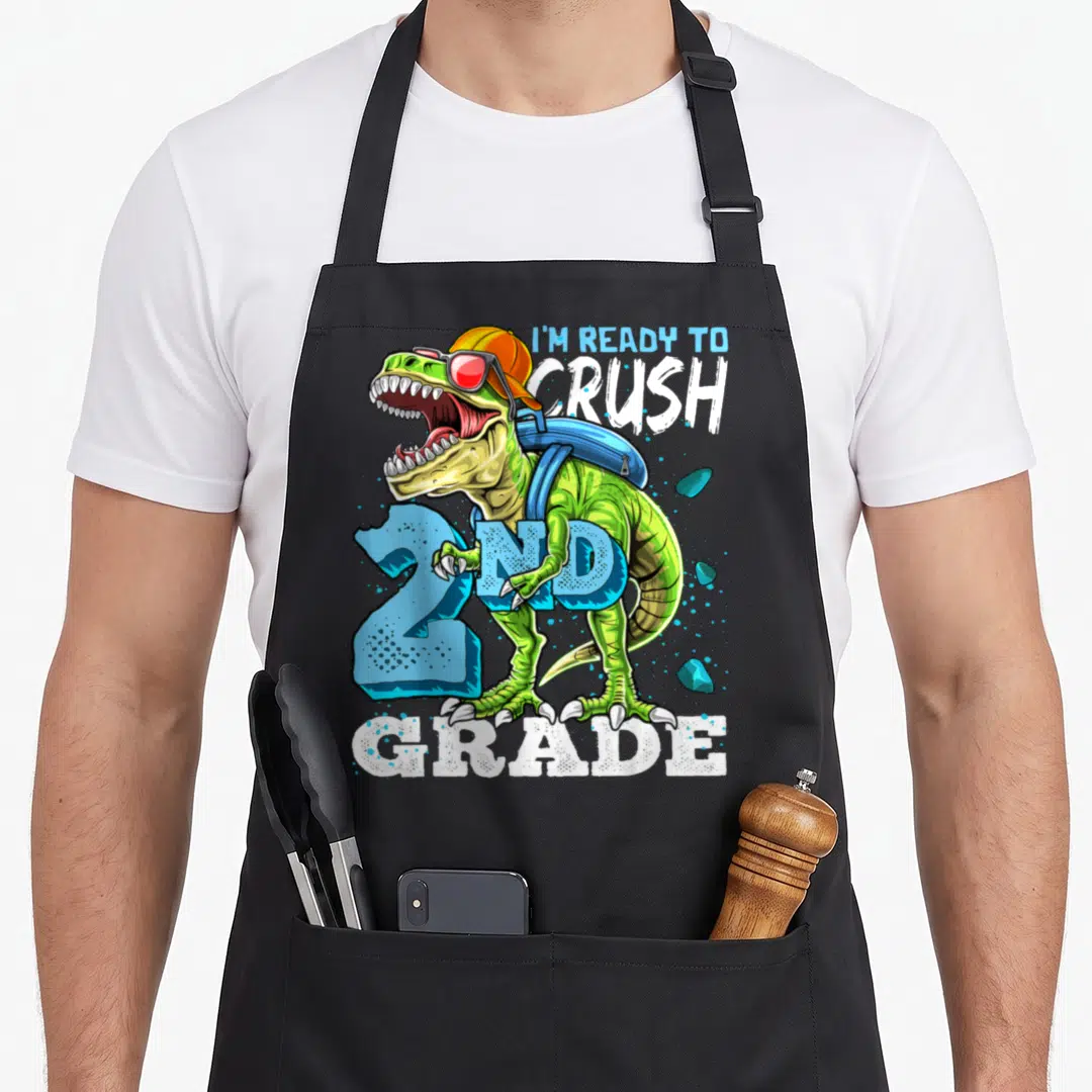 Ready 2nd apron - Green T-Rex with orange cap blue backpack and text I'm Ready To Crush 2nd Grade — shown on a black cotton canvas apron against a white background