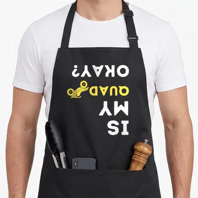 Okay biker apron - Vertical white and yellow text IS MY QUAD OKAY? with yellow quad bike icon — shown on a black cotton canvas apron against a white background