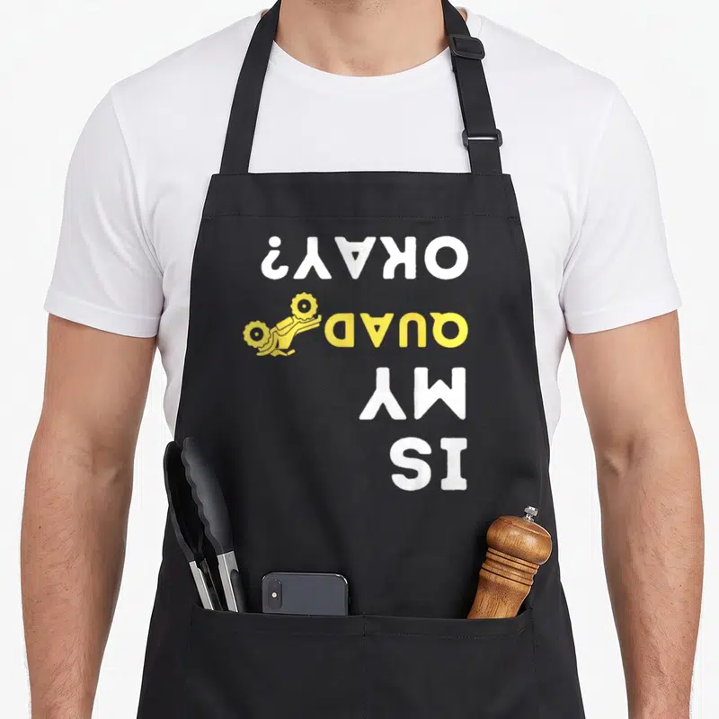 Okay biker apron - Vertical white and yellow text IS MY QUAD OKAY? with yellow quad bike icon — shown on a black cotton canvas apron against a white background