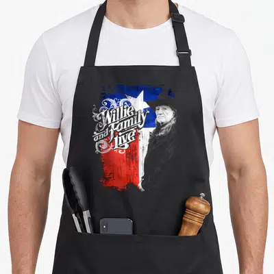 Willie texas apron - Willie Nelson portrait next to distressed Texas flag with swirling 'Willie and Family Live' text — shown on a black cotton canvas apron against a white background