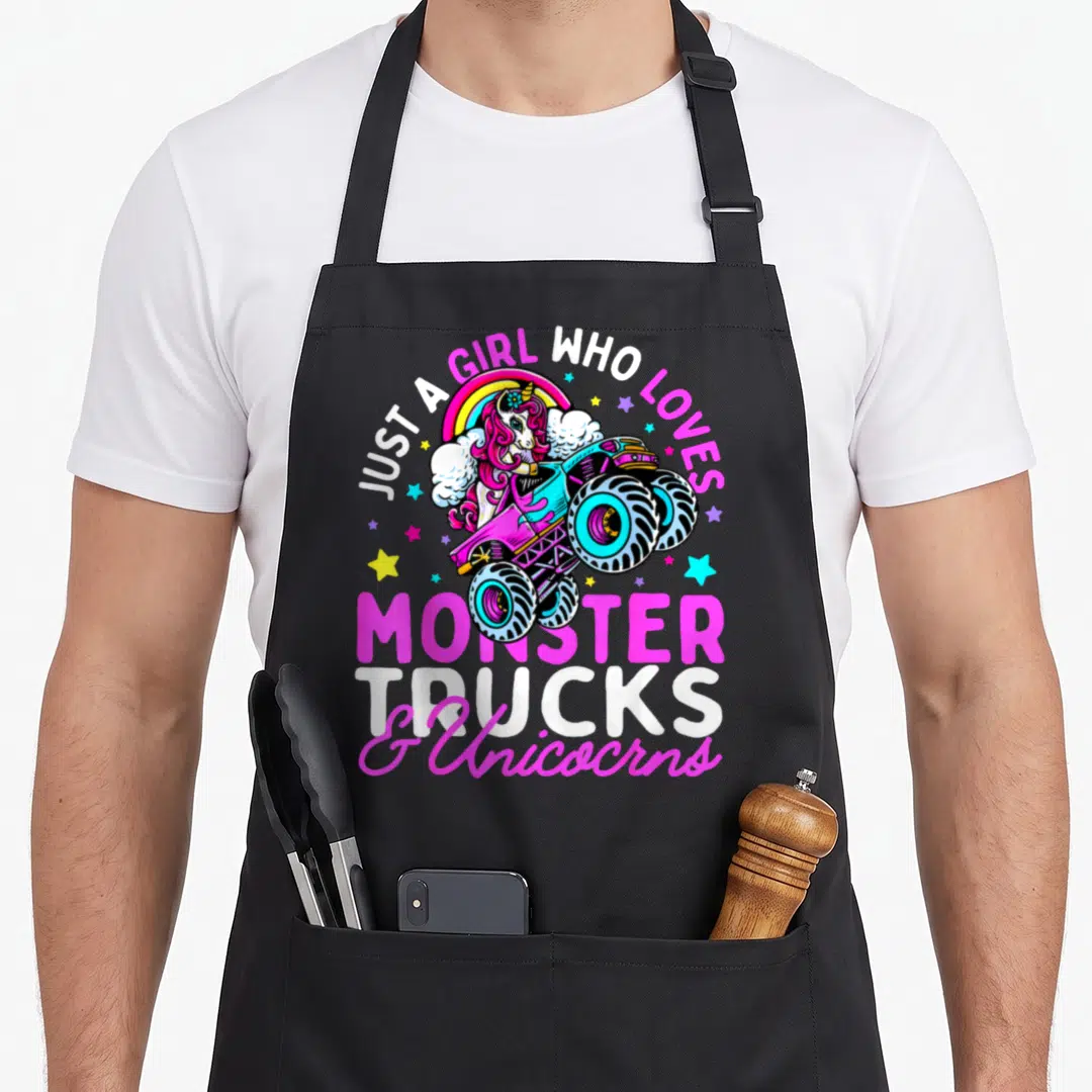 Monster unicorn truck aprons - Cartoon unicorn driving pink monster truck under rainbow with arched text and scattered — shown on a black cotton canvas apron against a white background