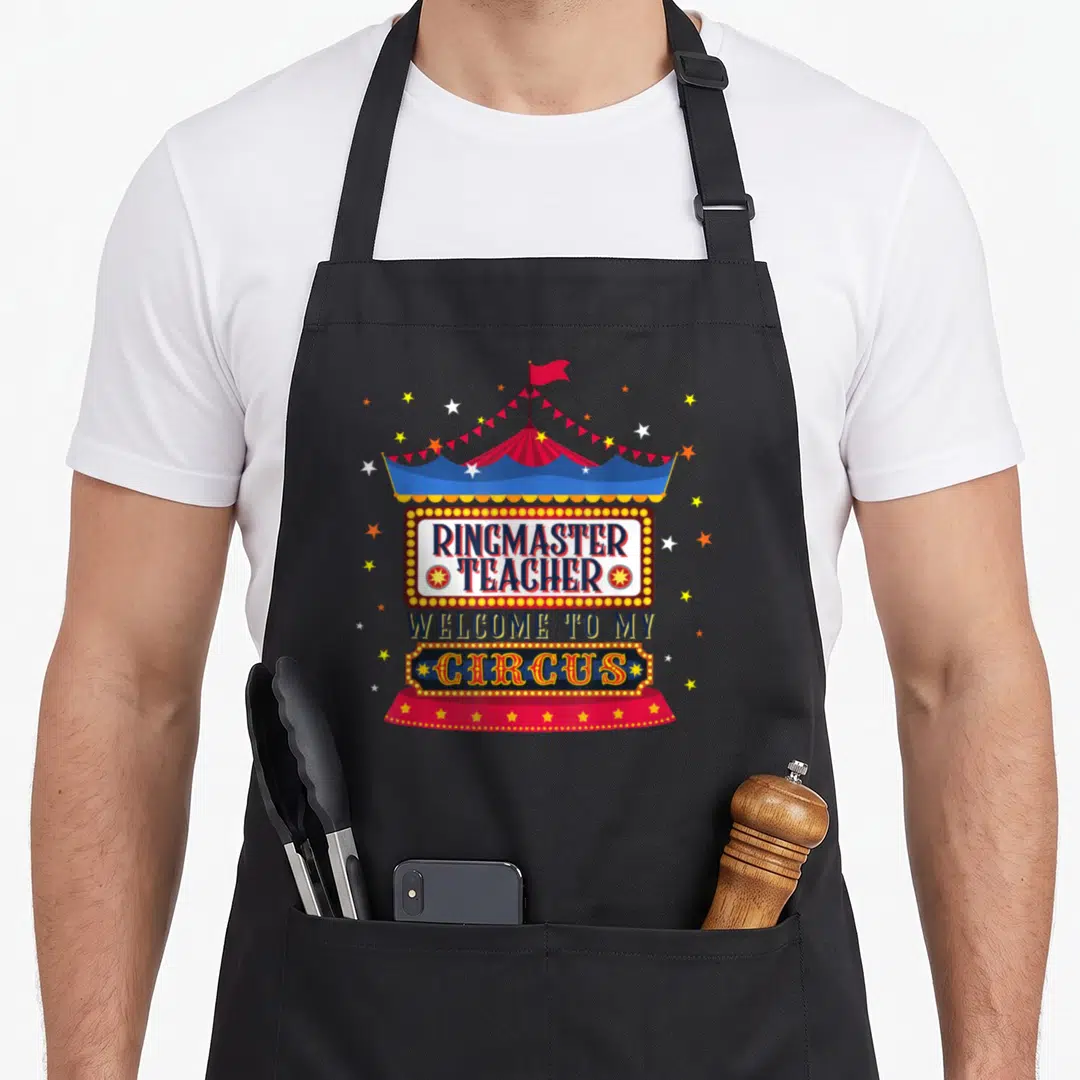 Ringmaster classroom aprons - Circus tent above marquee sign reading Ringmaster Teacher Welcome to My Circus with stars — shown on a black cotton canvas apron against a white background