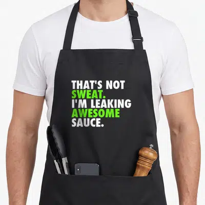 Sweat funny sauce apron - Stacked white and lime green text reading That's Not Sweat I'm Leaking Awesome Sauce — shown on a black cotton canvas apron against a white background