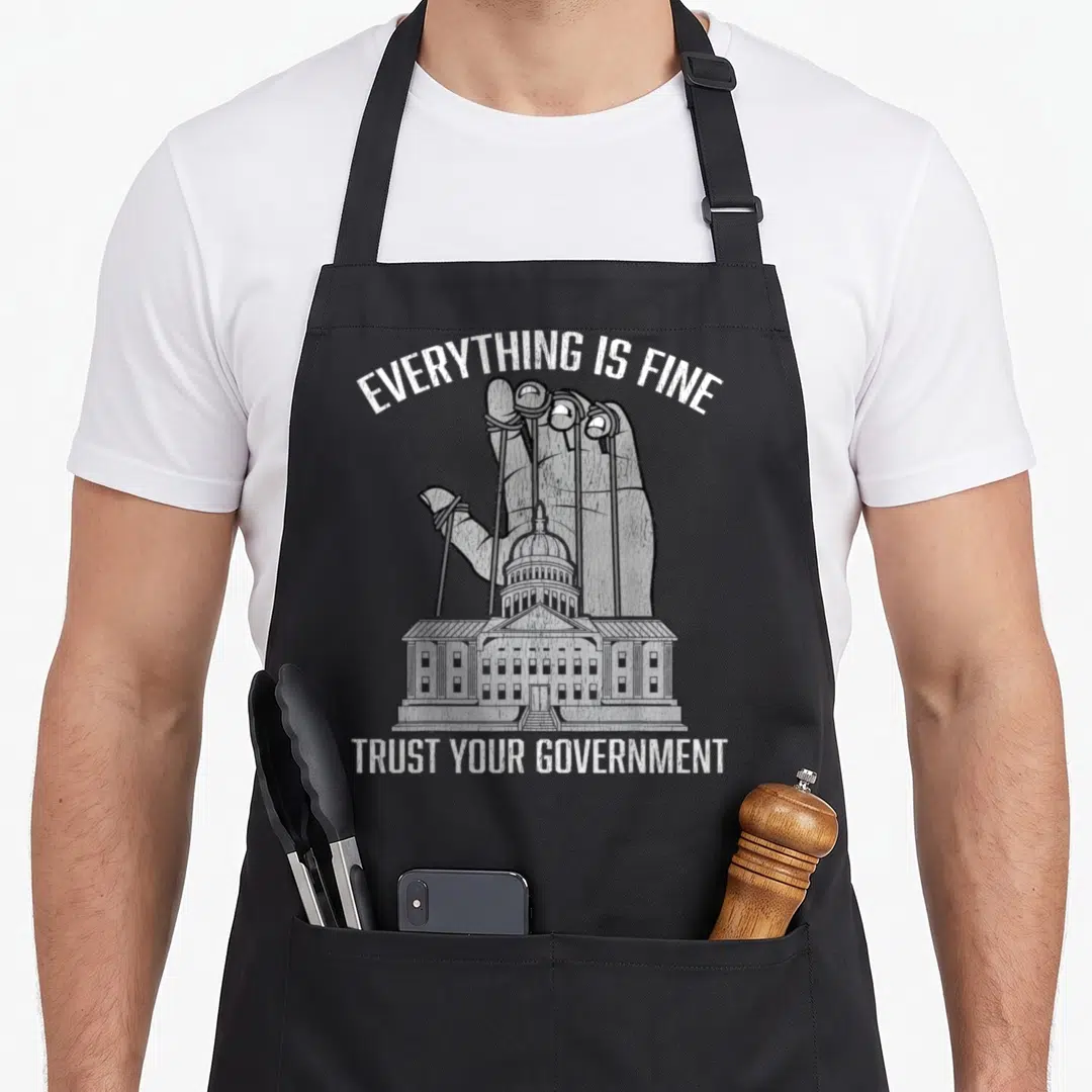 Fine conspiracy apron - Giant hand puppeting government building with Everything Is Fine Trust Your Government text — shown on a black cotton canvas apron against a white background